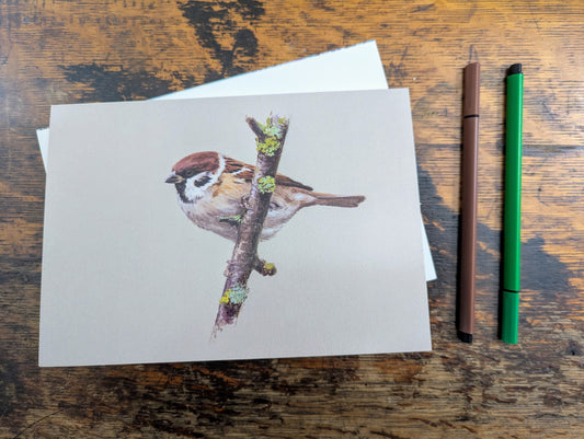 Card with a bird illustration on a wooden surface with two pens.