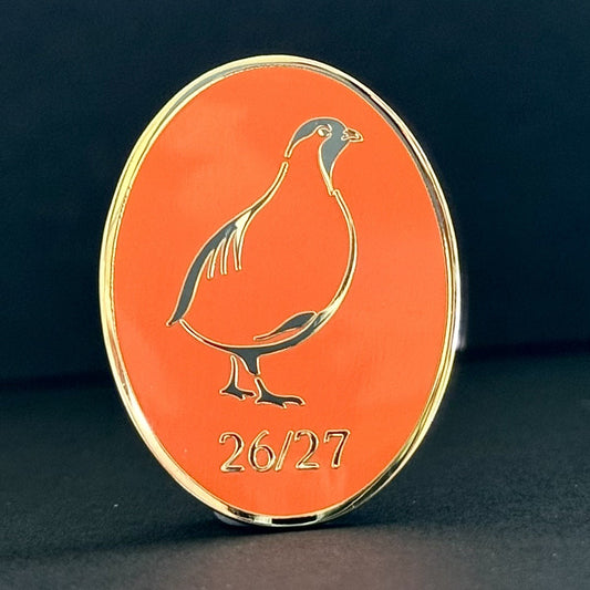 An oval orange collectible coin or medallion with a gold-plated border, featuring a gold bird silhouette and the text '26/27' at the bottom, set against a dark background.